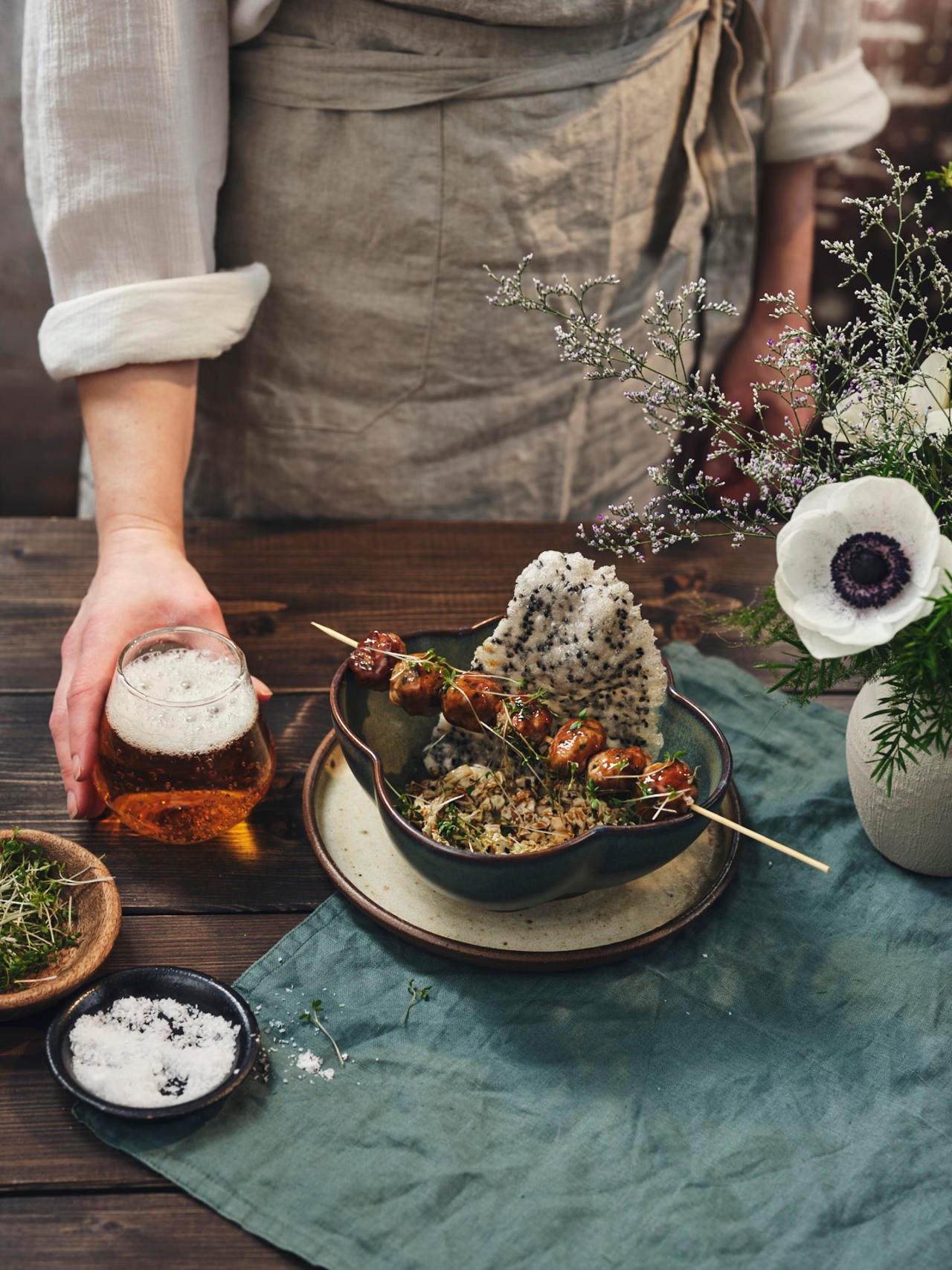 Servitören serverar ett glas öl till den japanska rätten "Niku Dango" som ligger på träbordet som är dekorerat med blommor
